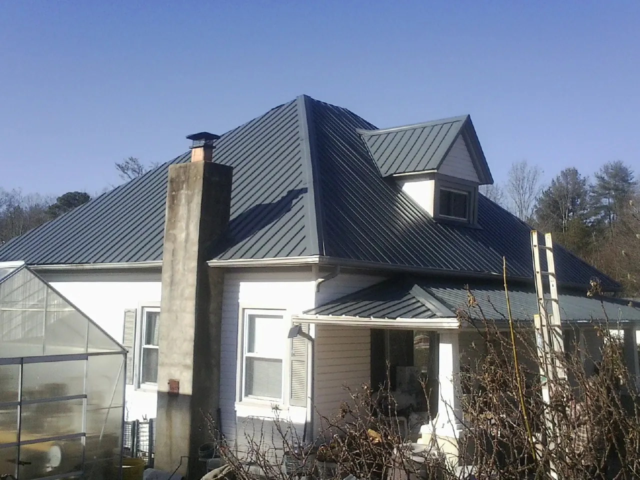 Dark blue standing seam metal roof on a white farmhouse with dormer — Slate & Tile Roof Repair by Roofing Brothers in Blairs
