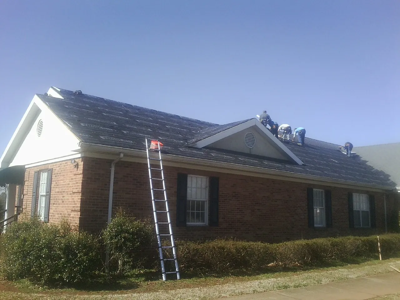 Crew tearing shingles off a brick ranch roof with a ladder set — Emergency Roof Repair work by our crew in Blairs
