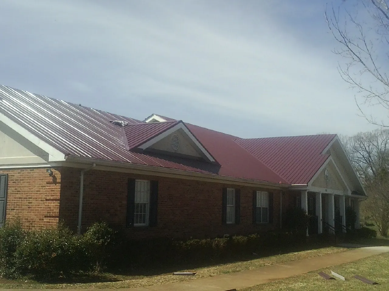 Red metal roof with gabled entries on a long brick building, from a Hail Damage Roof Repair job in Blairs