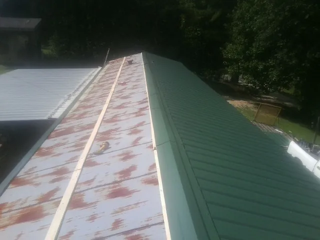Old rusted panels beside newly installed green metal roofing — Wind Damage Roof Repair by Roofing Brothers in Blairs