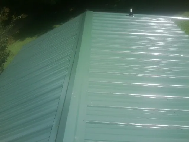 New green metal panels meeting at the ridge of a roof — Flat Roof Repair work by our crew in Blairs