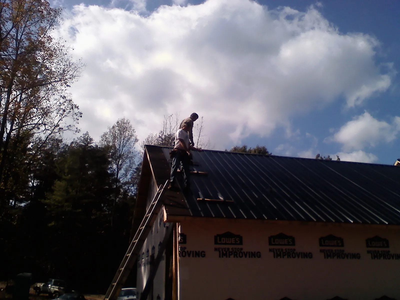 Roofer fastening dark metal panels high against a cloudy sky, from a Roof Inspection job in Blairs